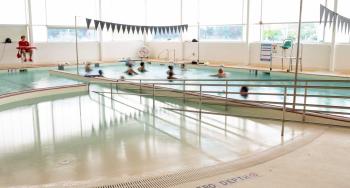 Image shows pool with zero depth ramp entry. In one area of the pool there is a aqua-fitness class, the other area is very shallow for children to play.