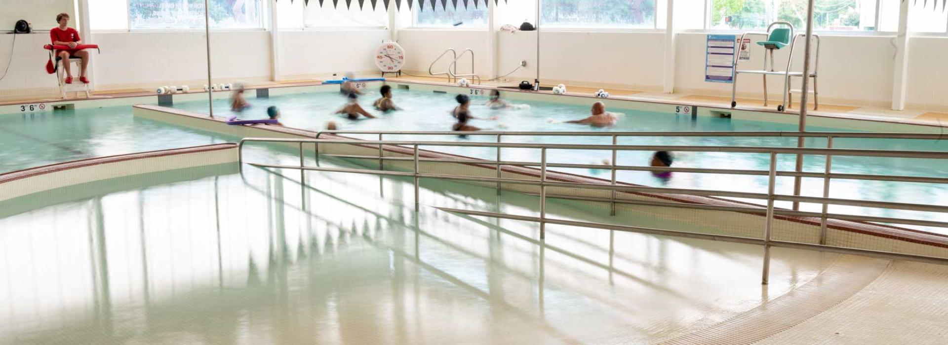 Image shows pool with zero depth ramp entry. In one area of the pool there is a aqua-fitness class, the other area is very shallow for children to play.